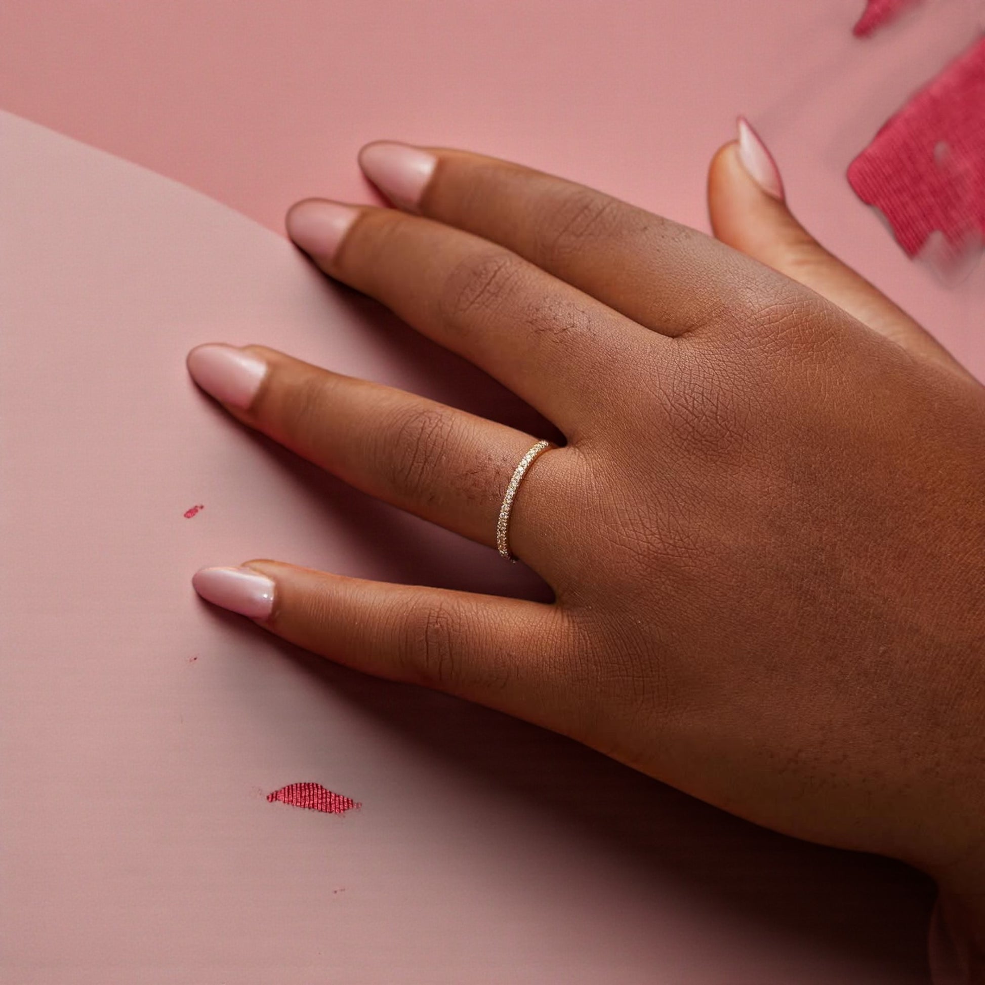 Hand wearing a gold ring on a pink background
