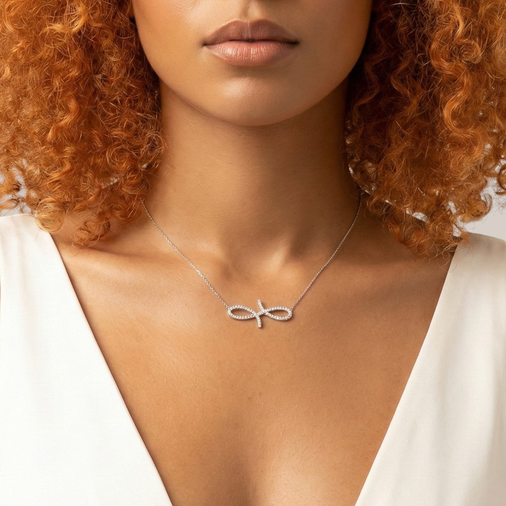 Woman wearing a silver necklace with an infinity symbol against a neutral background