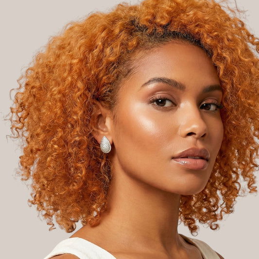 Woman with curly orange hair wearing earrings against a neutral background