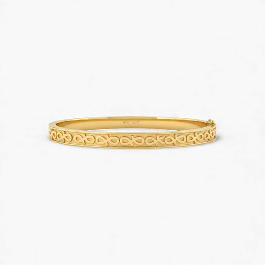 Gold bangle with intricate design on a white background