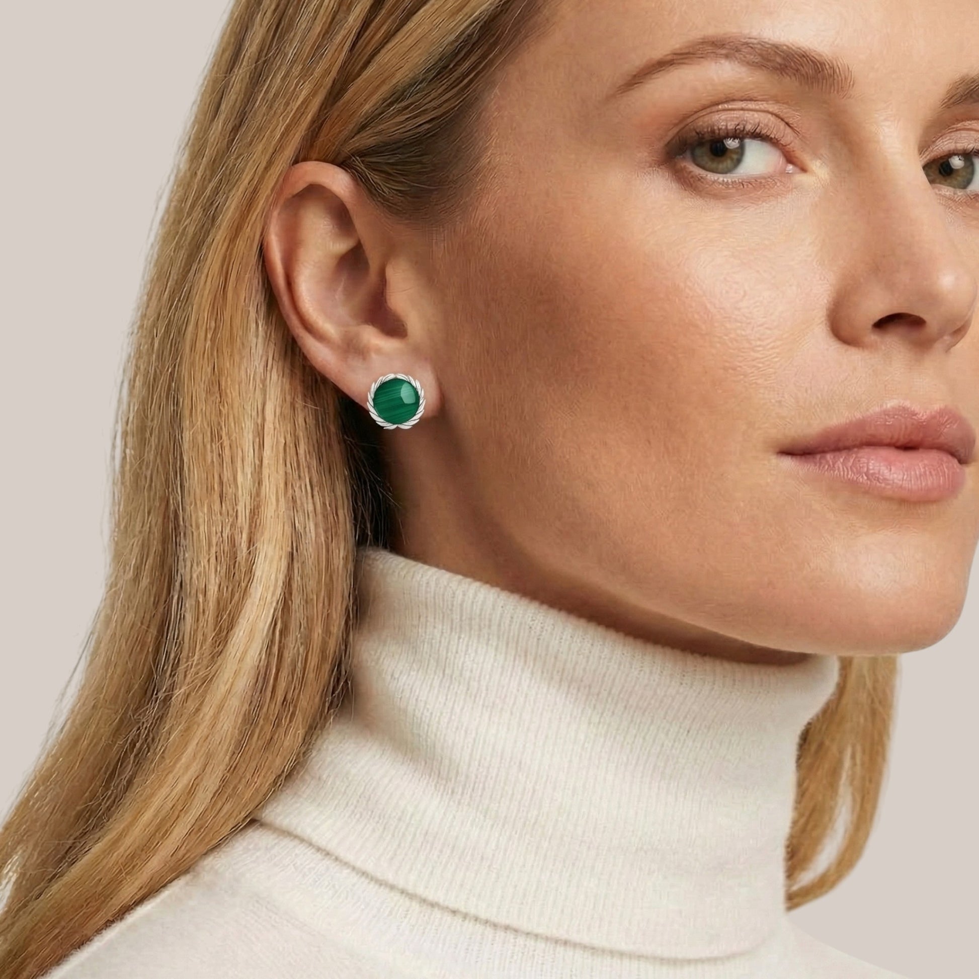 Close-up of a woman wearing green gemstone earrings with a neutral background