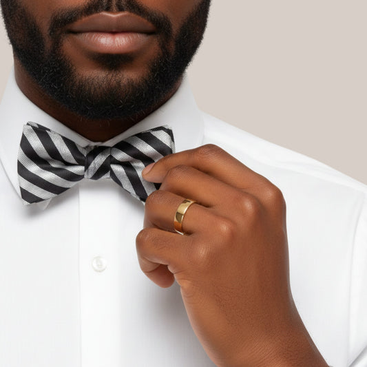 Man adjusting a black and white striped bow tie with a neutral background