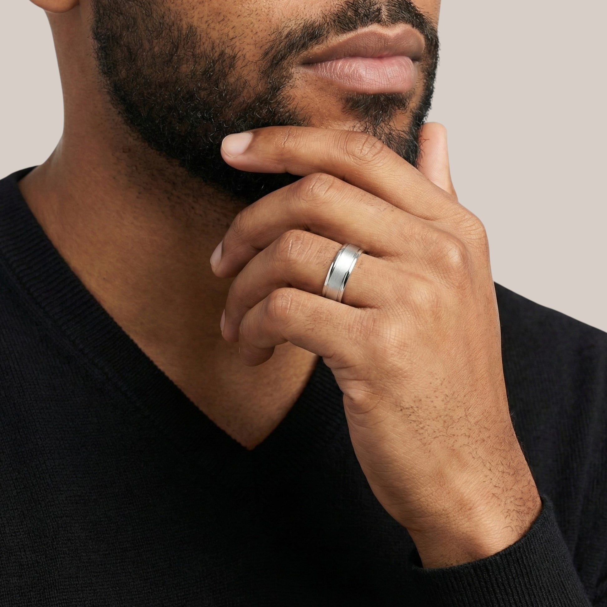 Man wearing a silver ring on his finger with a neutral background