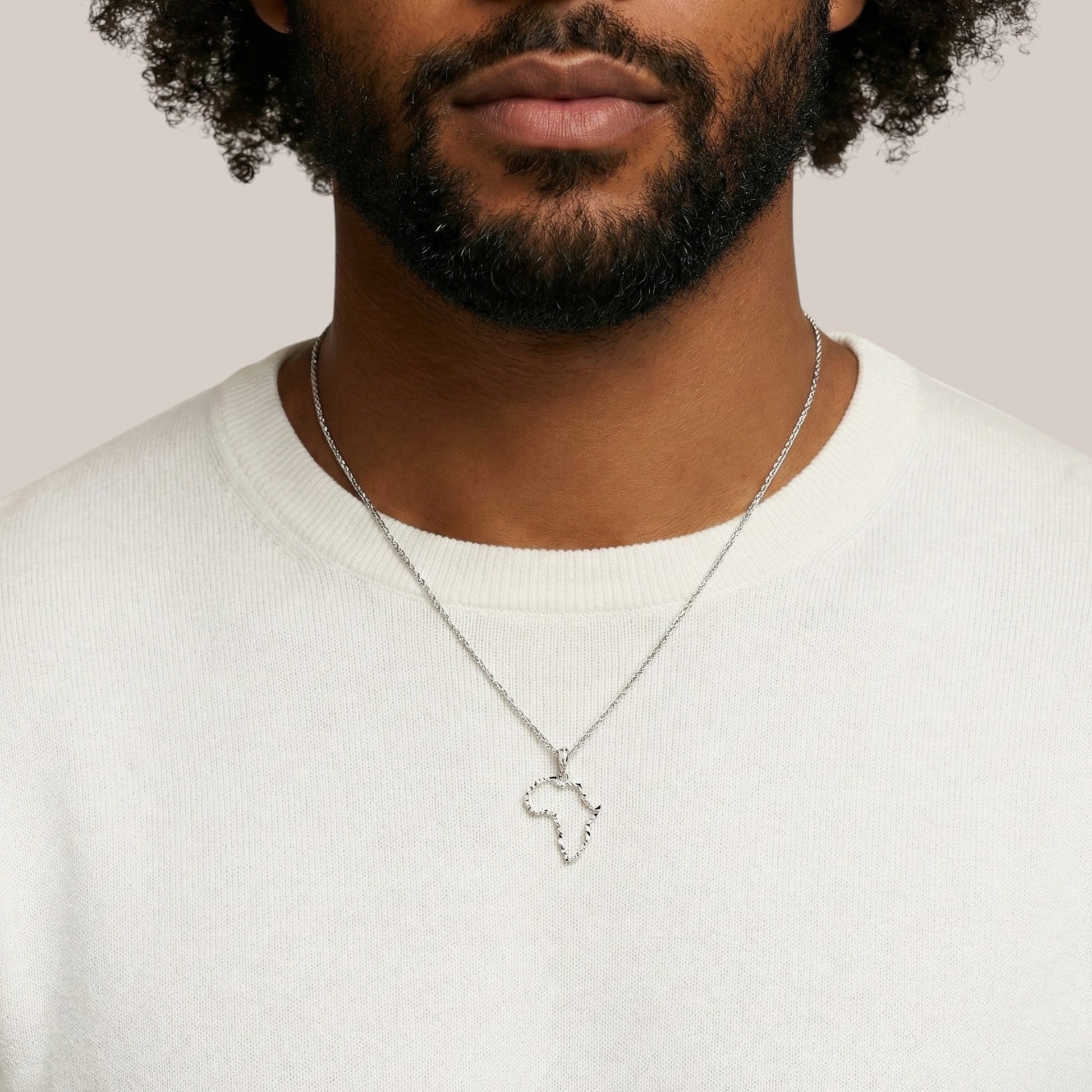 Man wearing a silver necklace with a heart-shaped pendant on a plain background