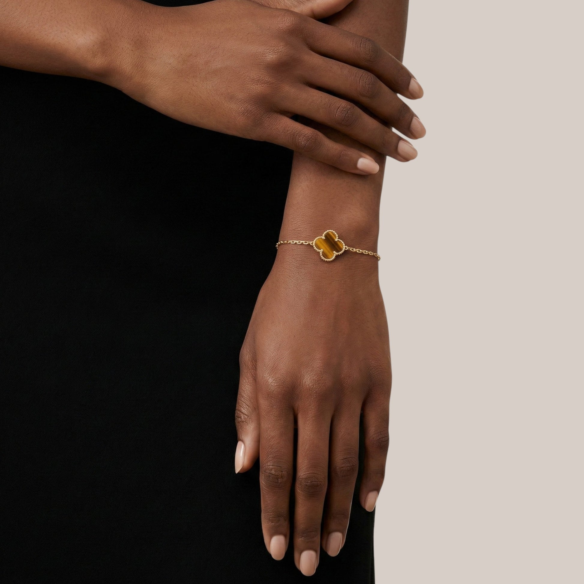 Gold bracelet with a clover design on a wrist against a neutral background