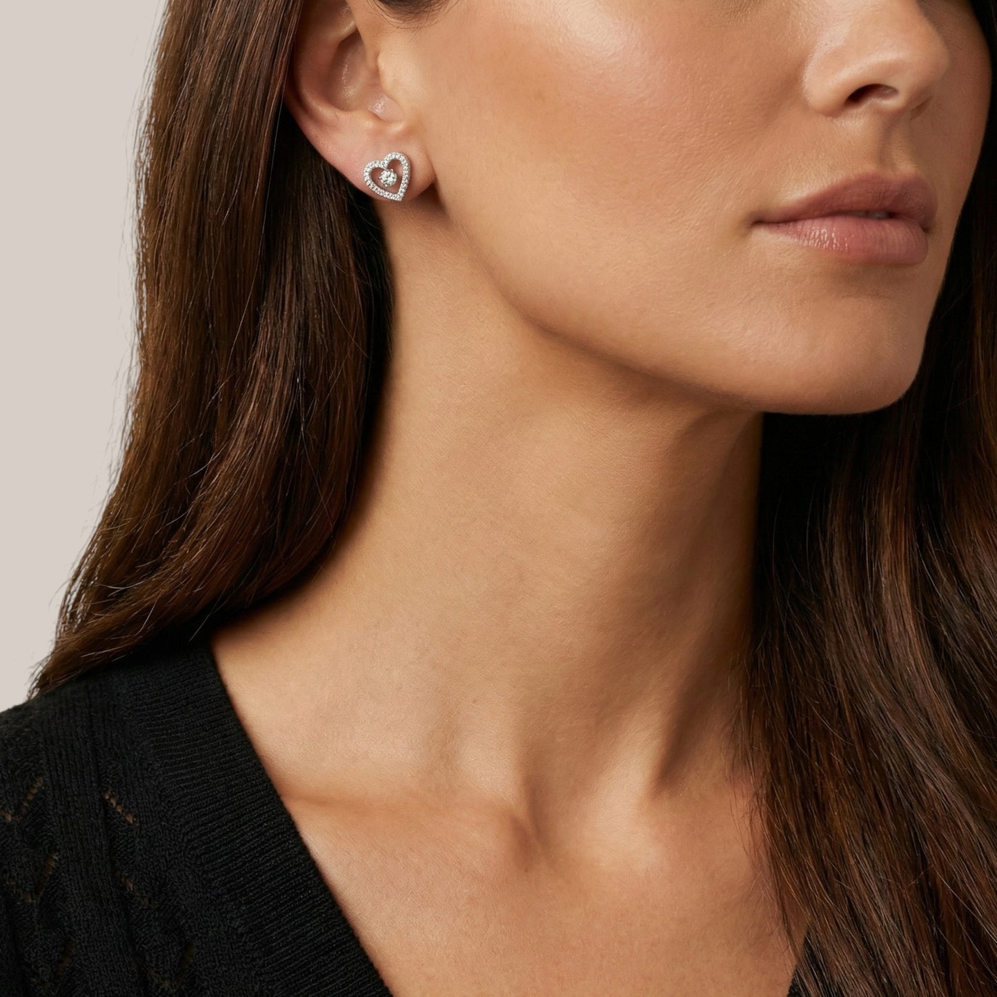 Close-up of a woman wearing heart-shaped earrings with a neutral background