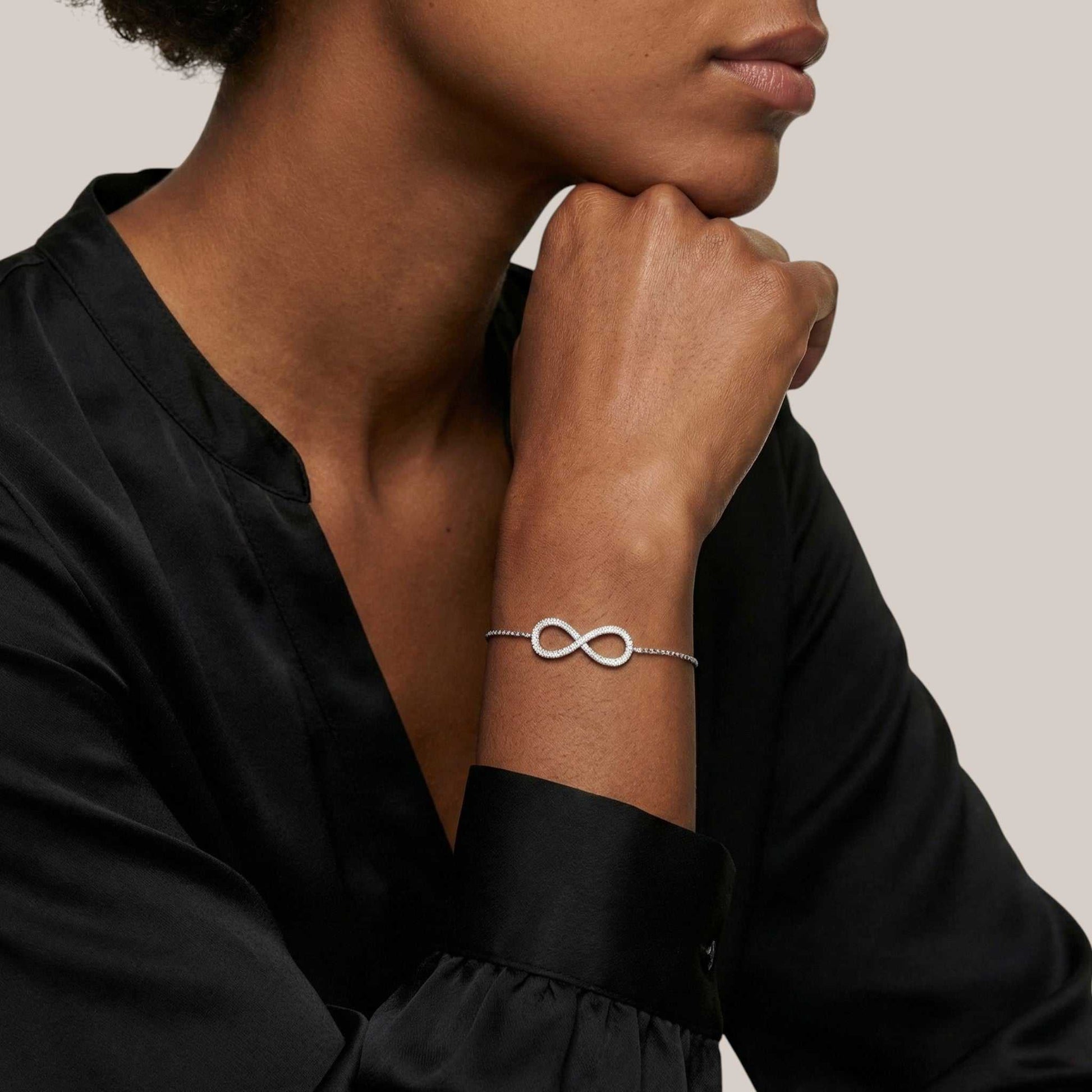 Person wearing a silver infinity bracelet on a neutral background
