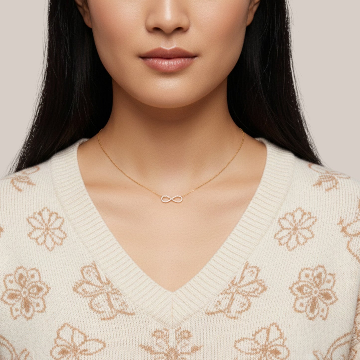 Woman wearing a gold necklace with an infinity symbol on a neutral background
