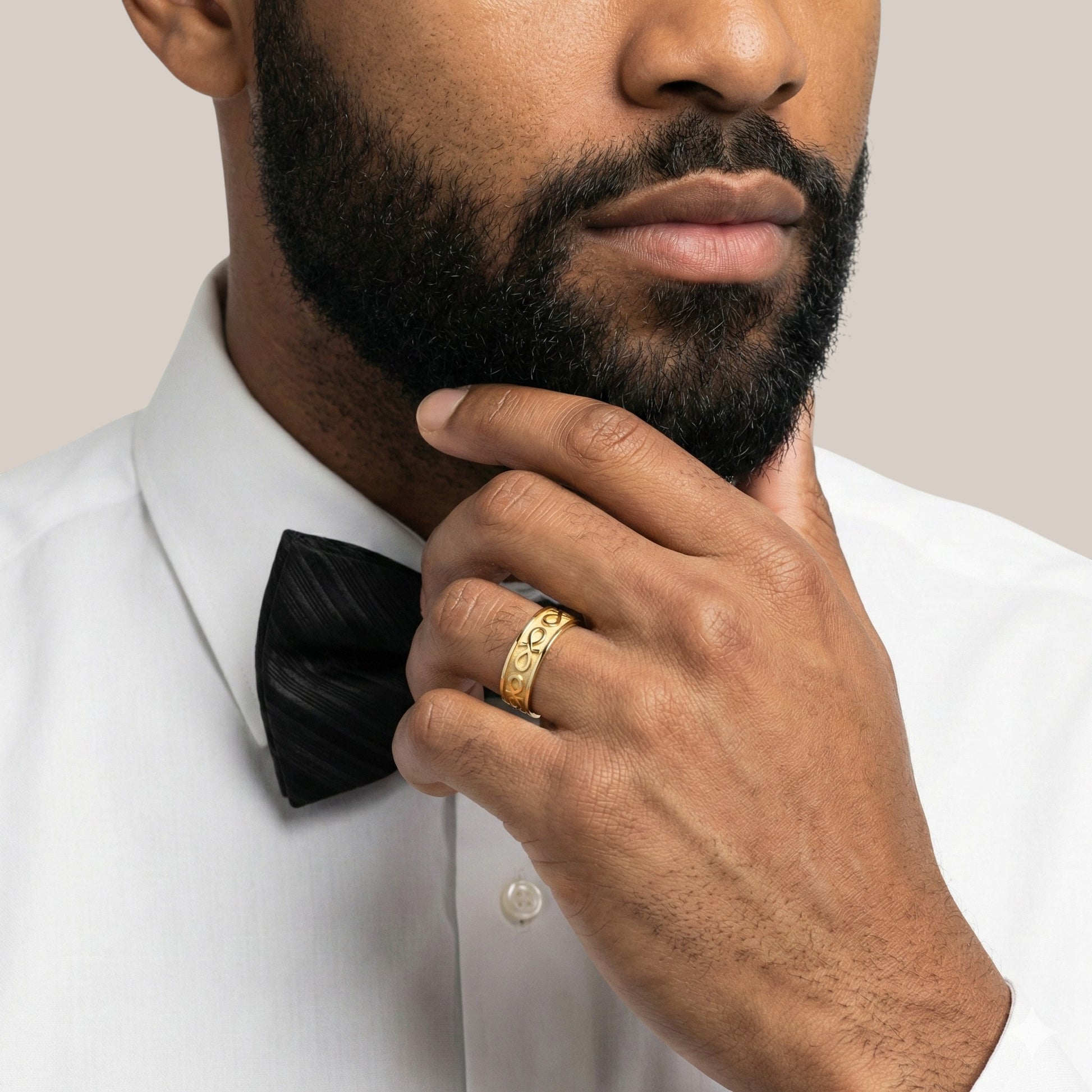 Man wearing a white shirt with a black bow tie and a gold ring, against a neutral background