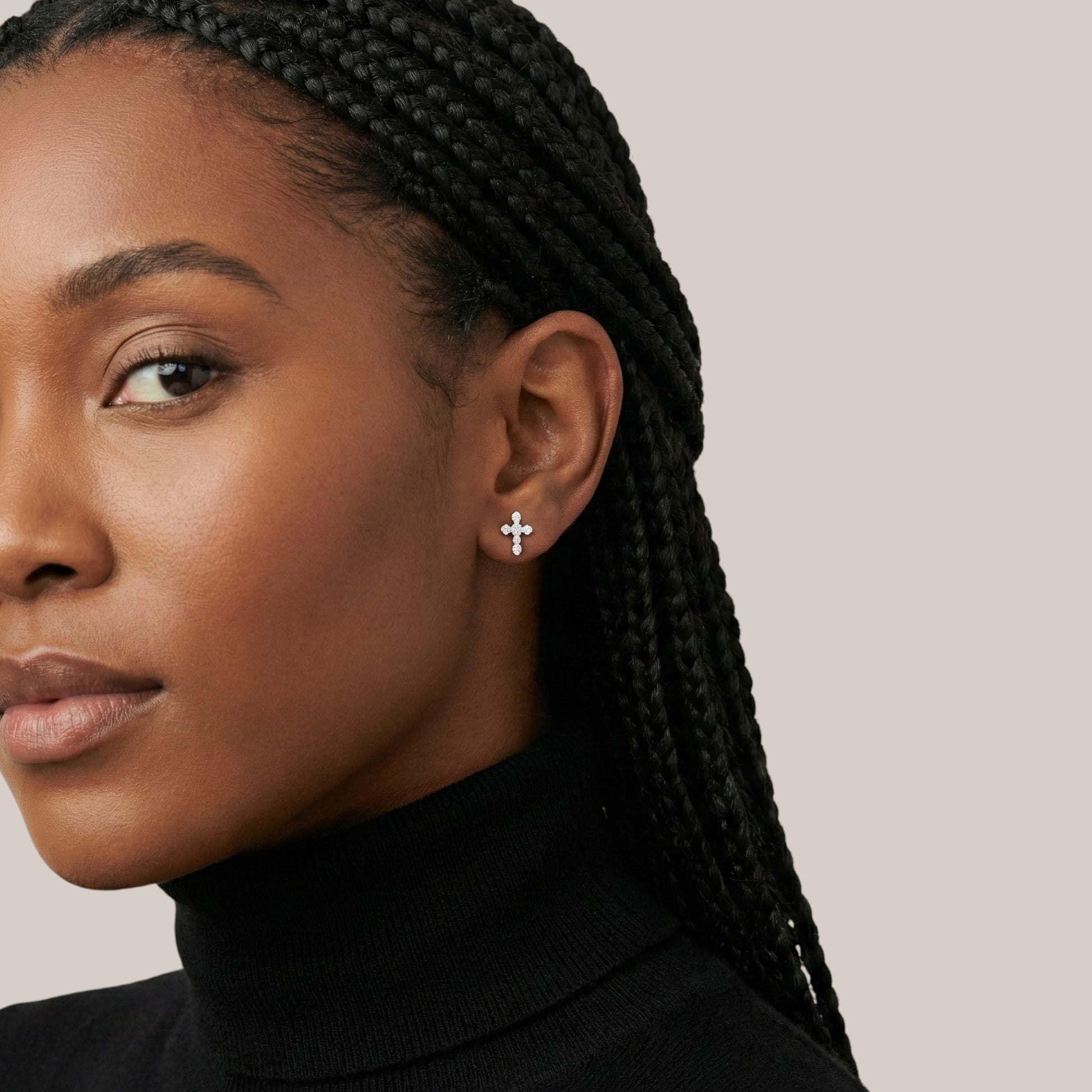 Close-up of a woman wearing a cross earring against a neutral background