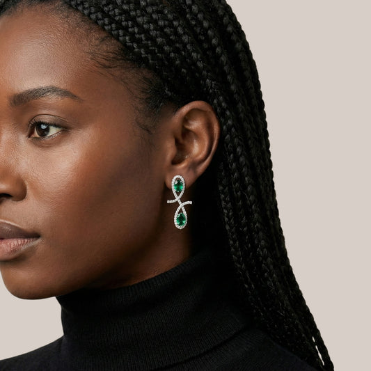 Close-up of a woman wearing green and silver earrings with braided hair.