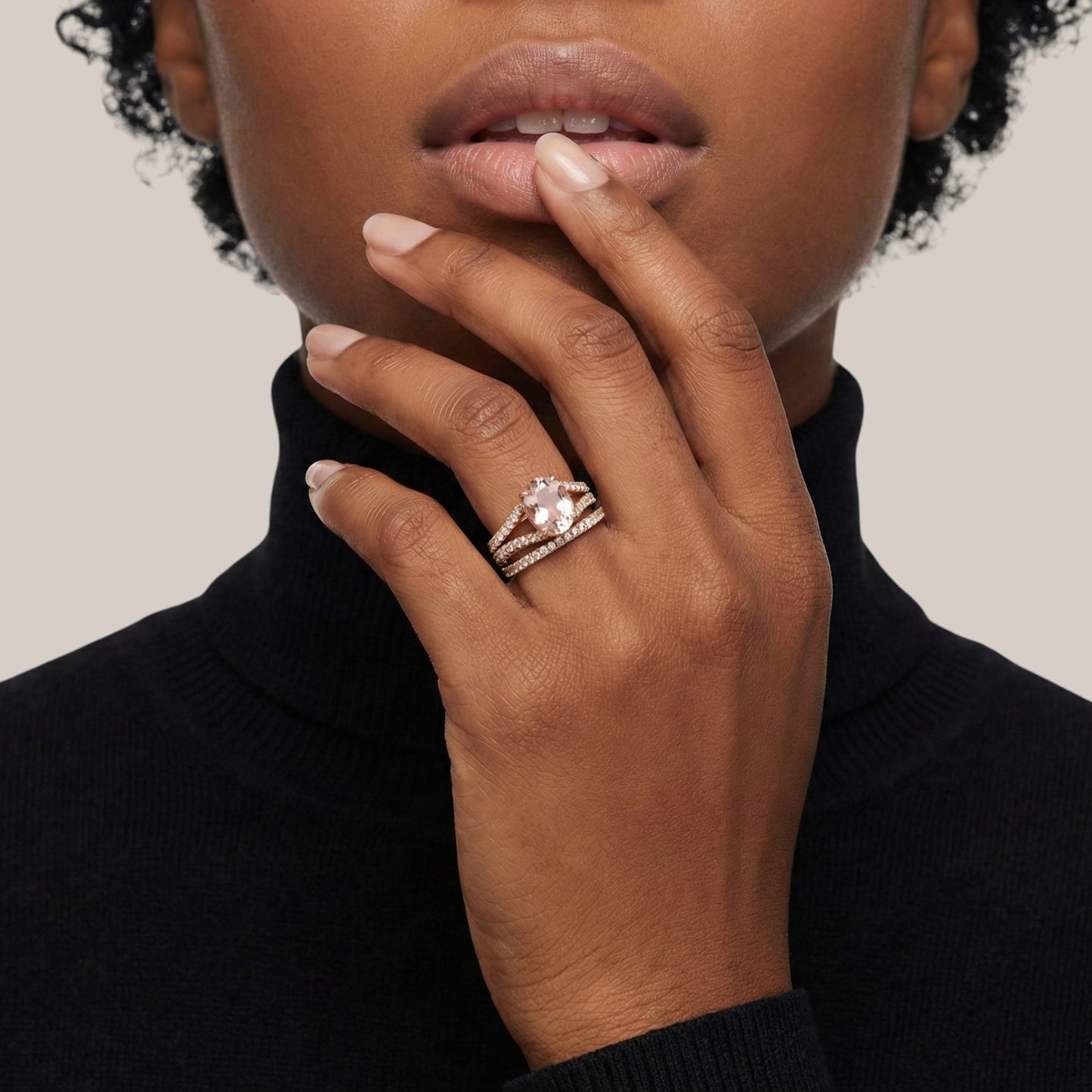 Close-up of a hand wearing a ring with a diamond, touching the chin against a neutral background