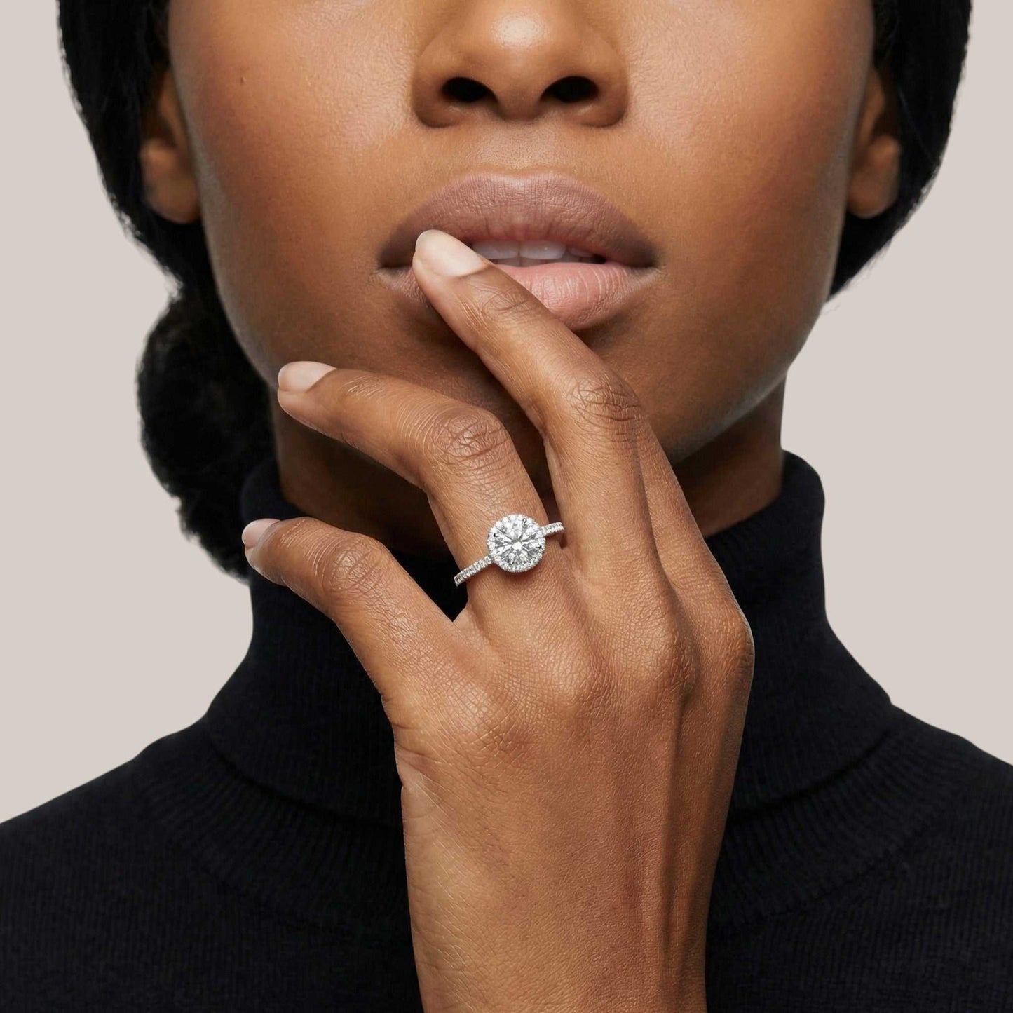 Close-up of a woman's hand wearing a diamond ring with a neutral background