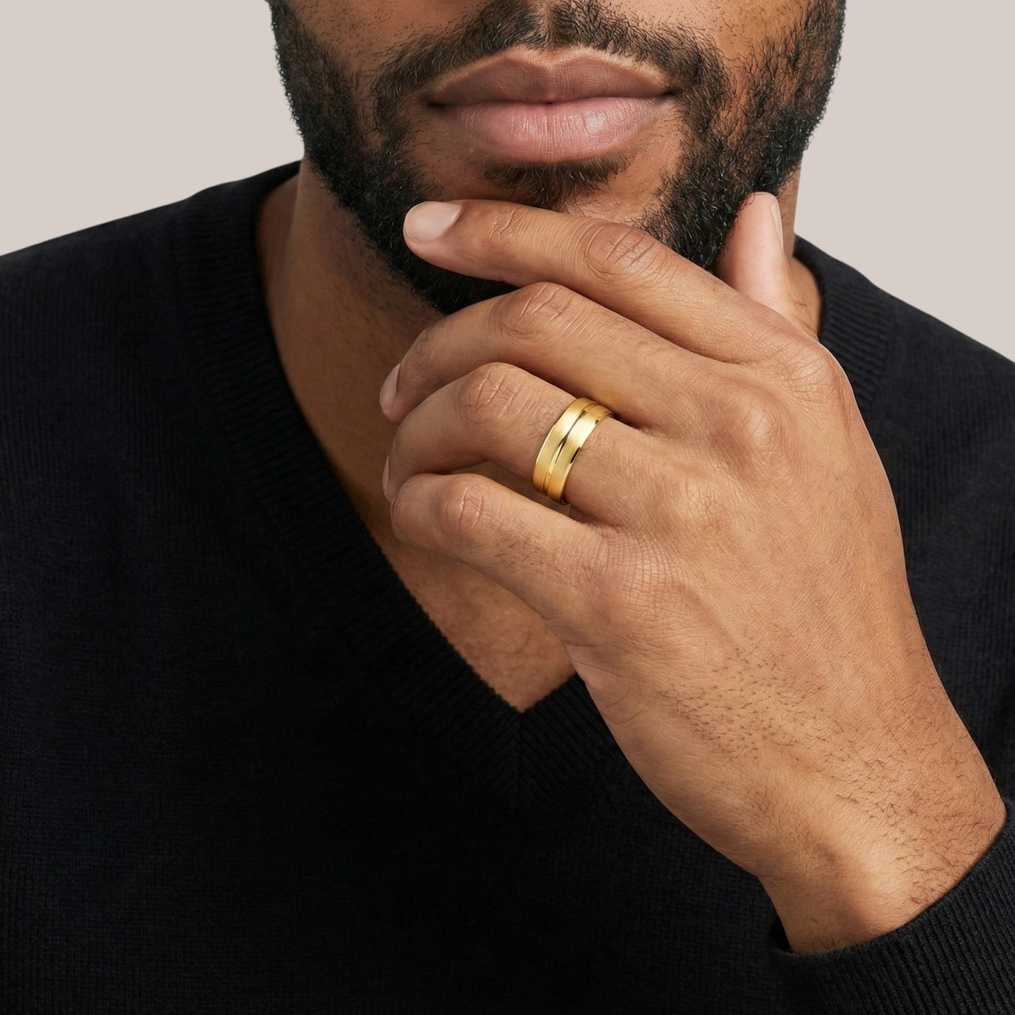 Man wearing a gold ring on his finger with a neutral background