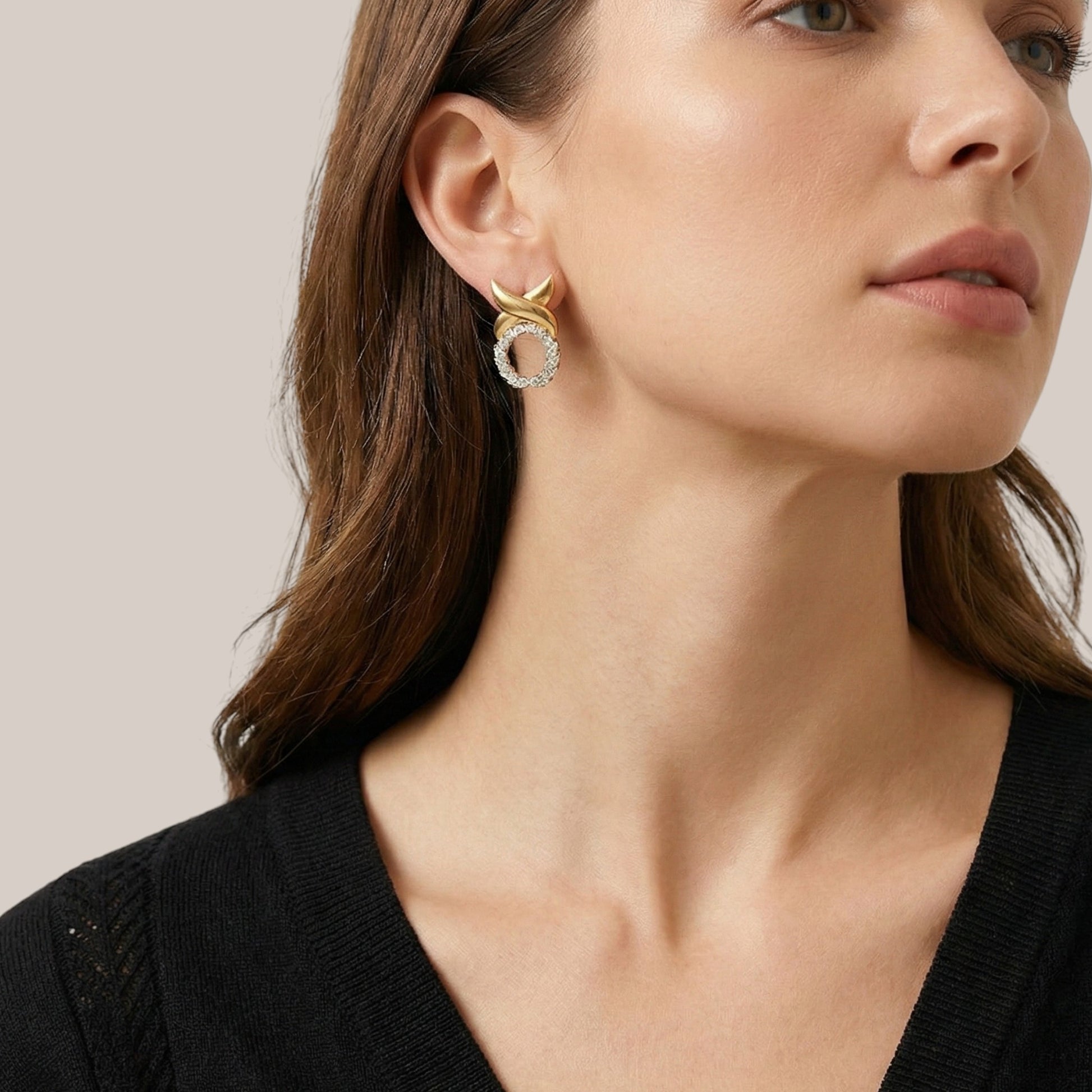 Close-up of a woman wearing gold hoop earrings against a neutral background