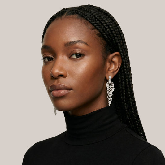 Woman with braided hair wearing a black turtleneck and silver earrings on a neutral background