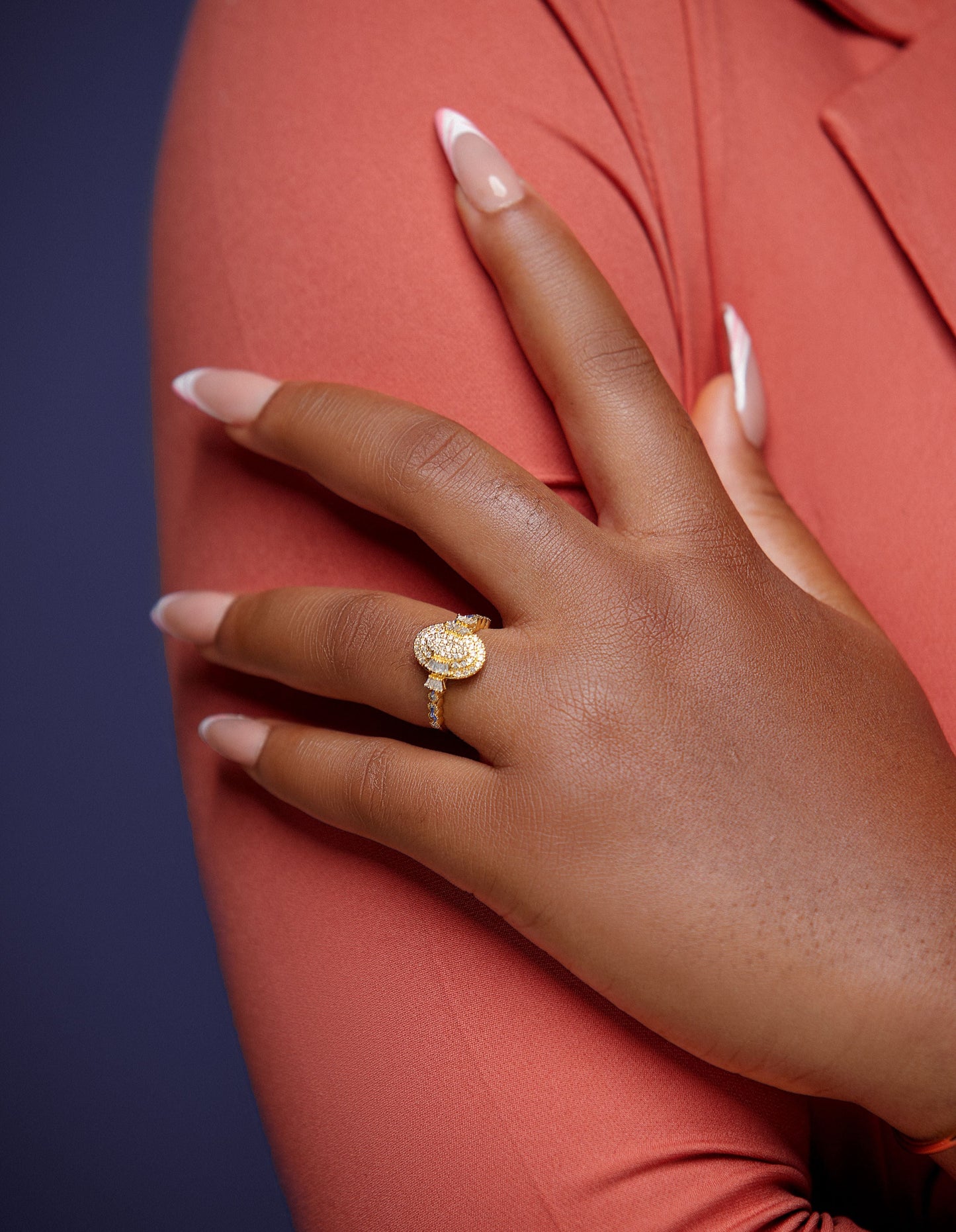 Hand wearing a gold ring on a pink garment against a dark background