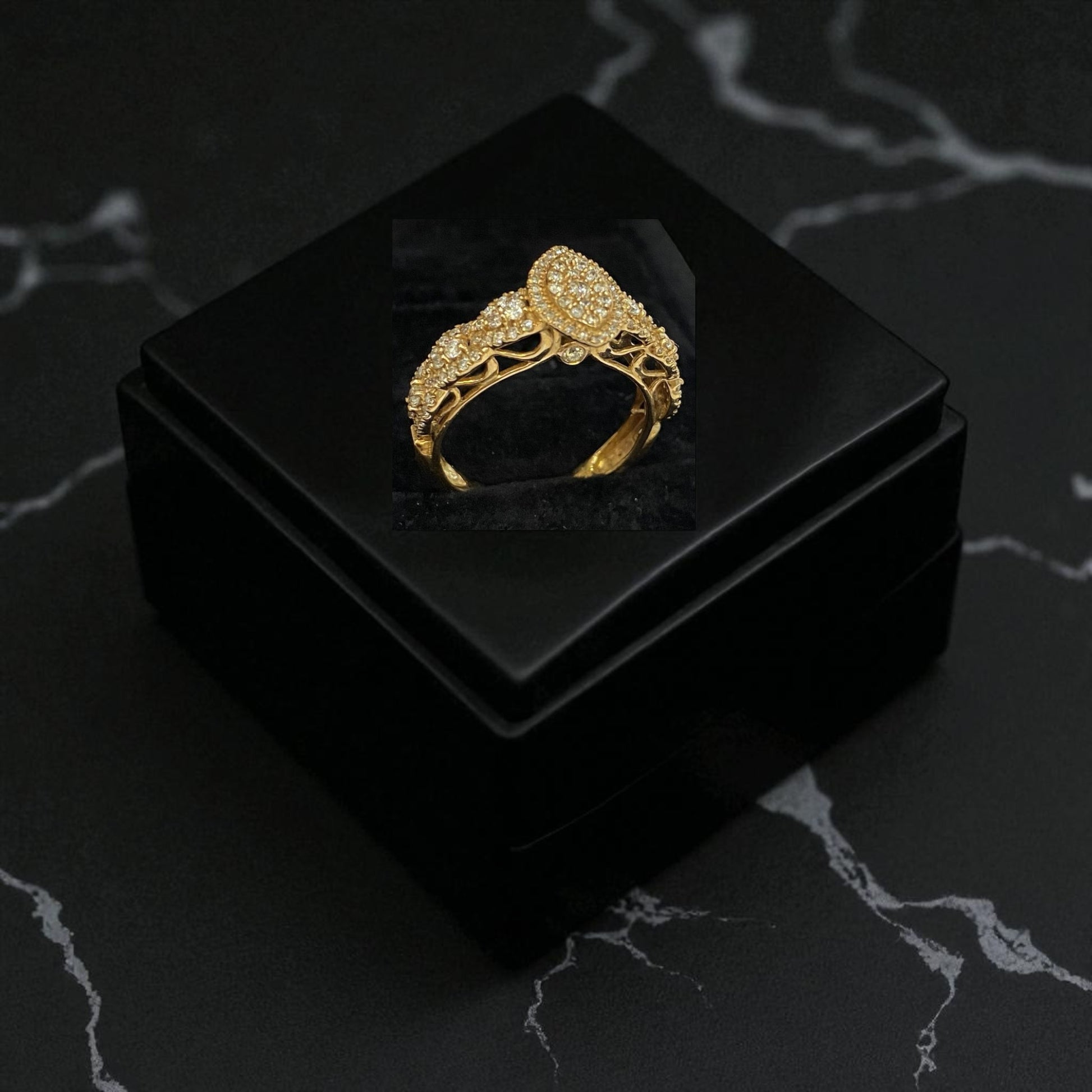 Gold ring with intricate design on a black jewelry box against a dark marble background