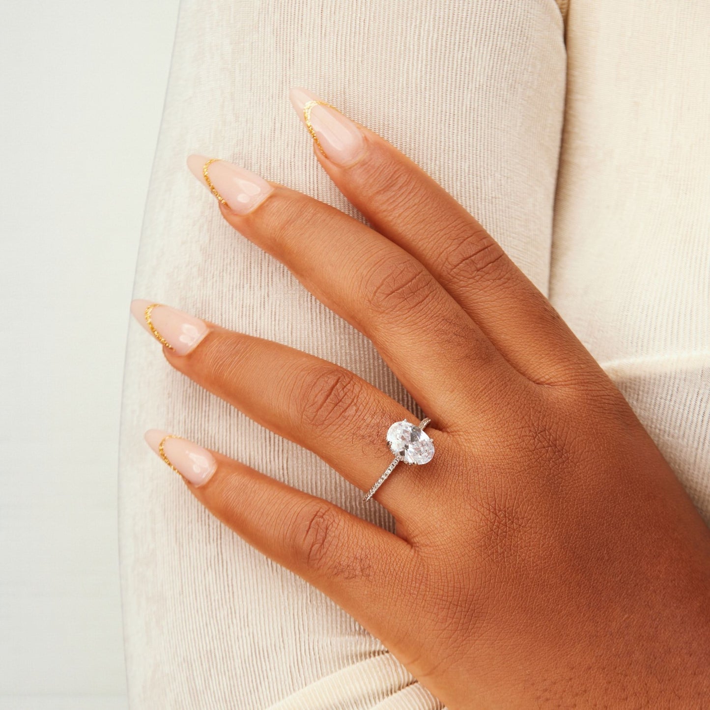 Hand wearing a diamond ring on a neutral background