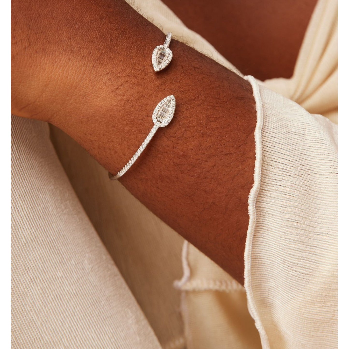 Silver leaf-shaped bracelet on a wrist with a neutral background