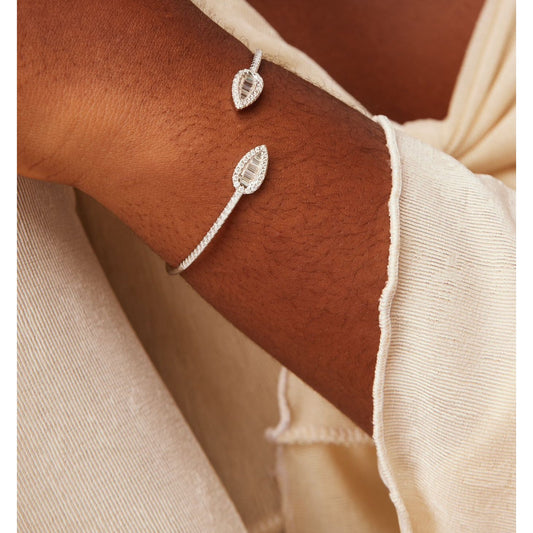 Silver leaf-shaped bracelet on a wrist with a neutral background