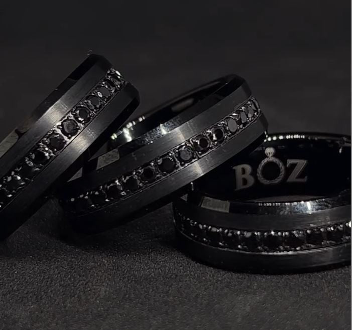Two tungsten carbide bands with black sapphire accents, one with the inside of the band visible showing the sapphires, the other showing the outside with the word 'BOZ' on the band.