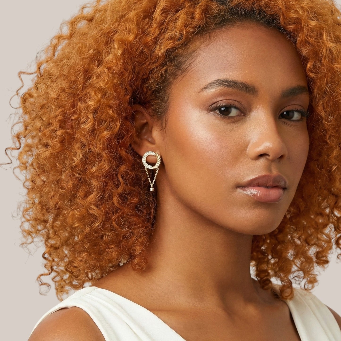 Woman with curly orange hair wearing a white top against a neutral background