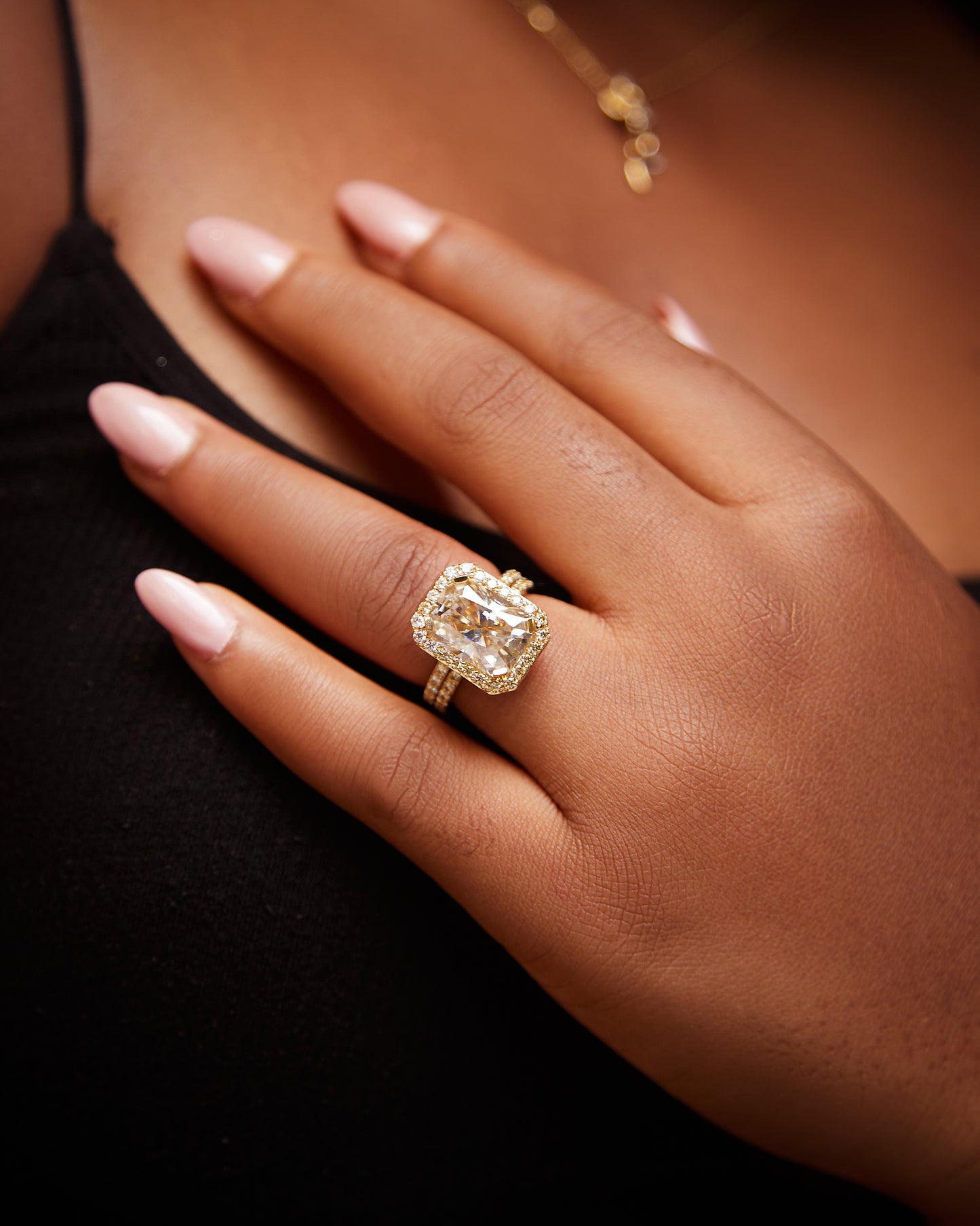 Hand wearing a gold ring with a large diamond on a blurred background