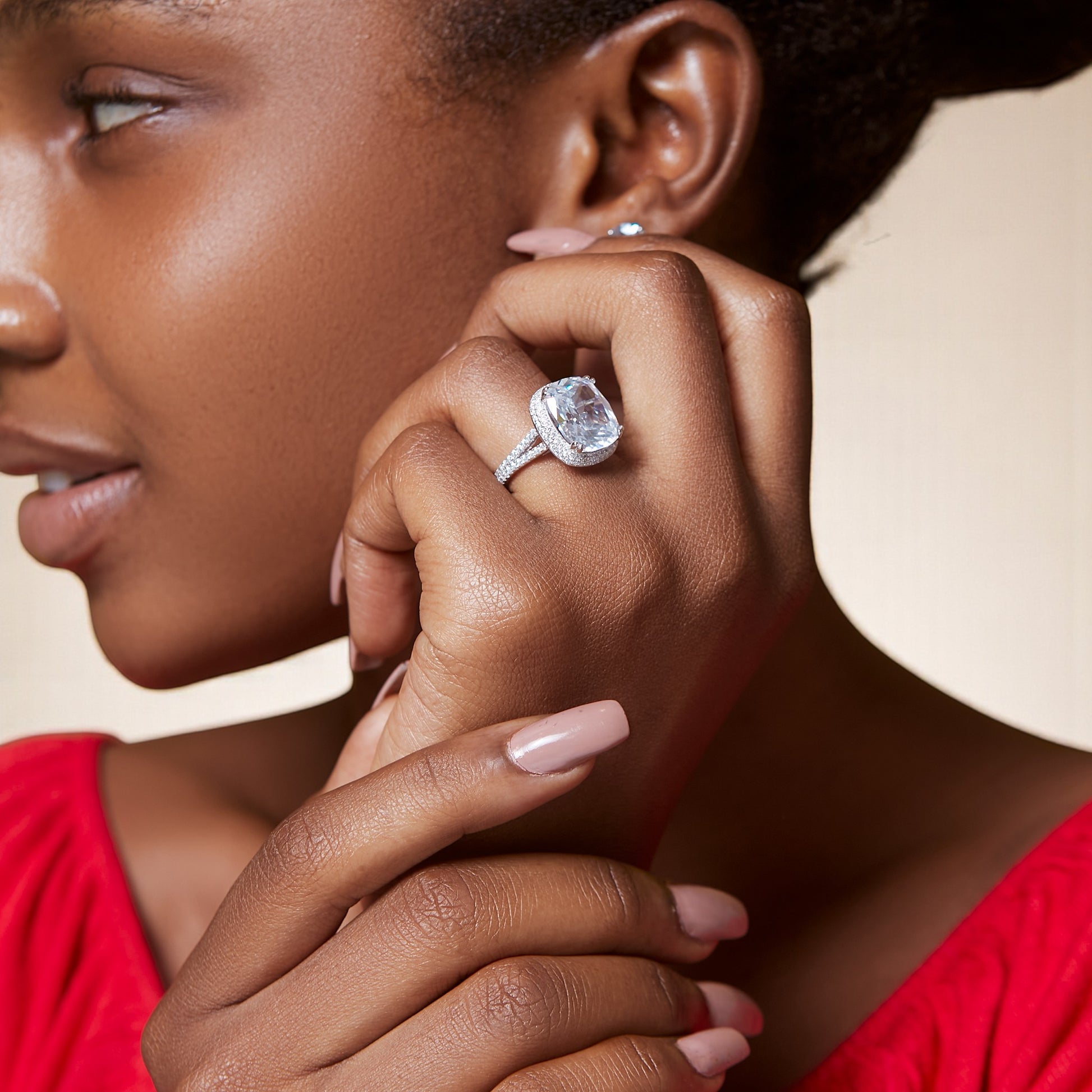 Close-up of a woman wearing a diamond ring on her finger against a neutral background