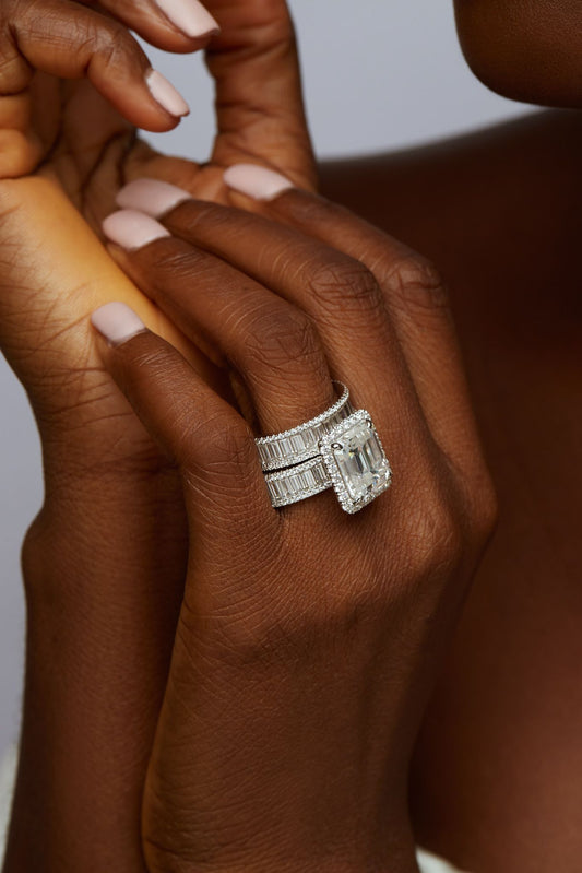 A person's hand with a ring on the finger, indicating the engagement ring is part of a bridal set.