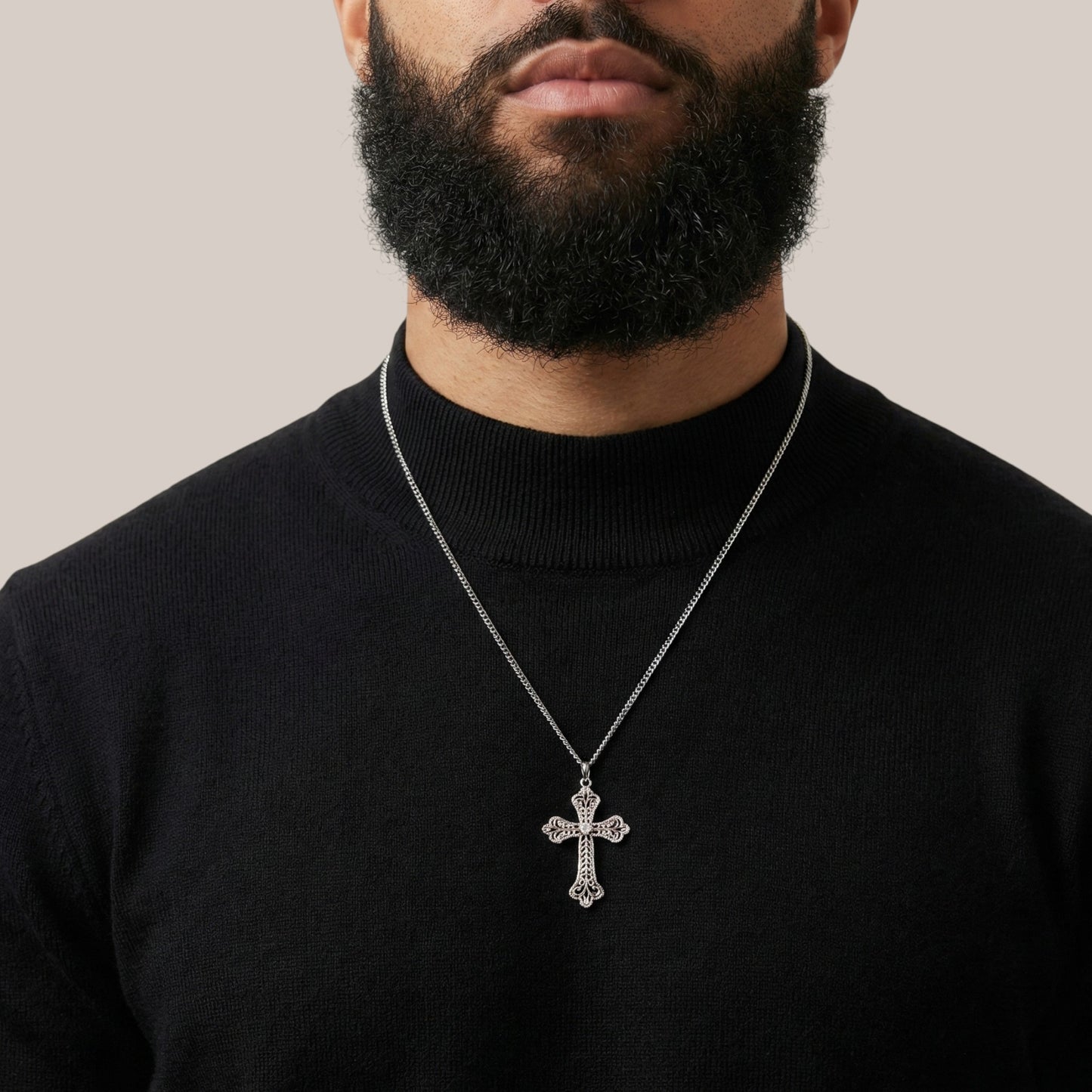 Man wearing a black turtleneck with a silver cross necklace against a neutral background